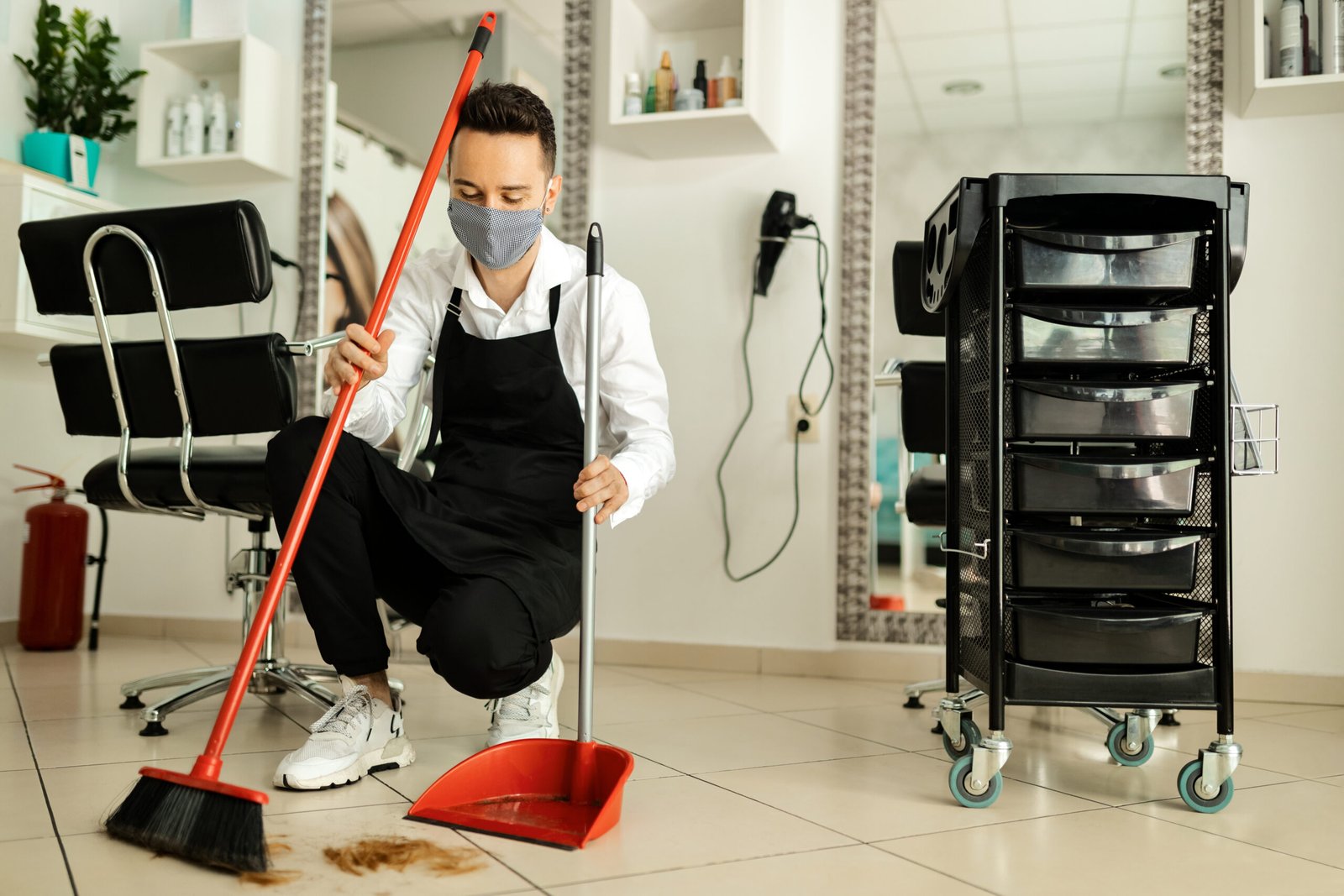 hairdresser with protective face mask cleaning salon after a hai